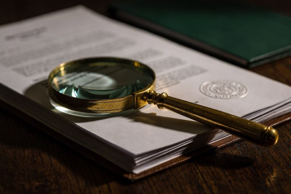 A magnifying glass resting on certification paperwork with an embossed seal